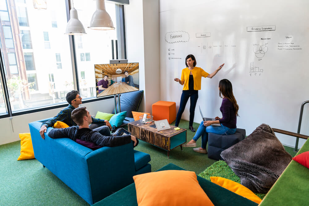 Ein Team arbeitet an einem entspannten Arbeitsplatz &uuml;ber das Room Kit mit anderen Teammitgliedern hybrid zusammen